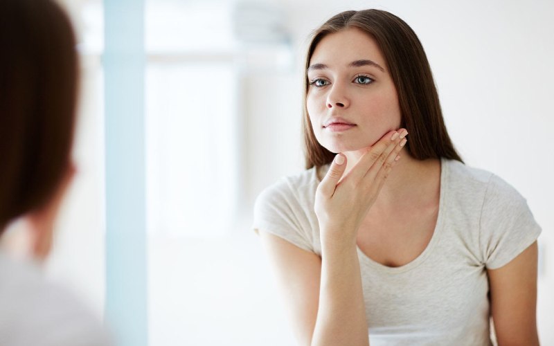 woman inspecting her skin in the mirror