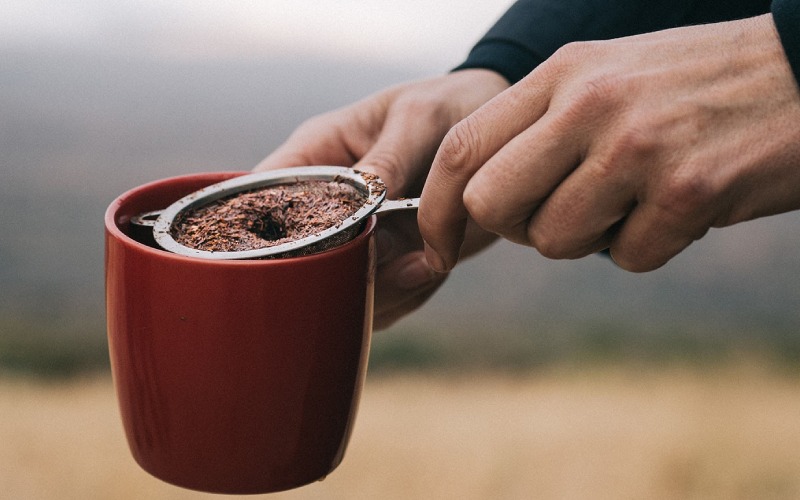 rooibos tea in strainer and red mug being held by a person